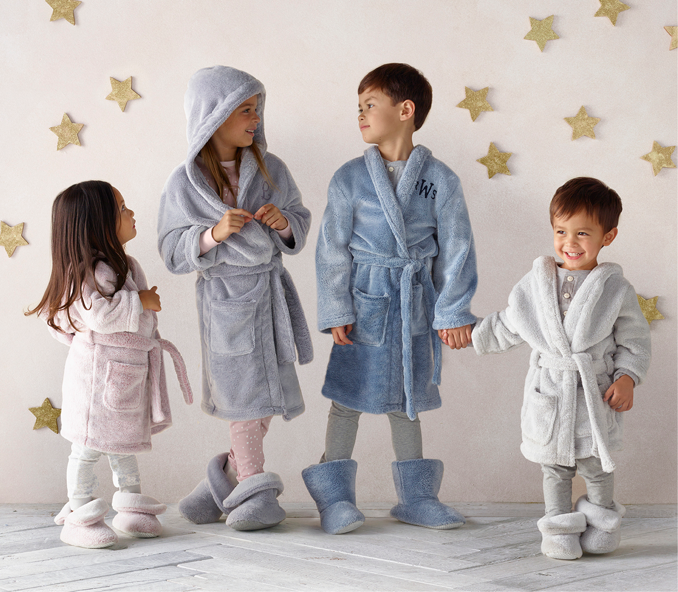 Four kids in fuzzy robes and slippers under a gold-star backdrop
