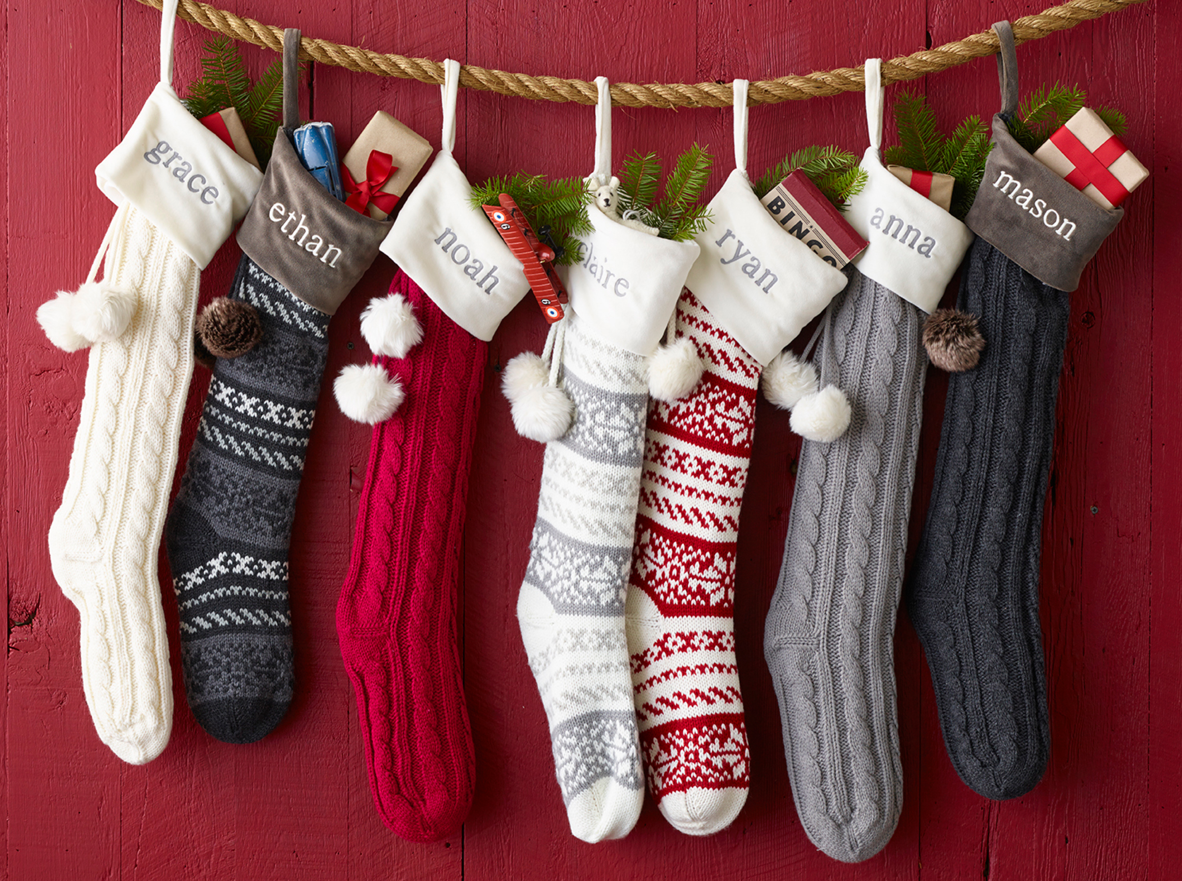 Personalized knit stockings hung on rope against a red barn wall